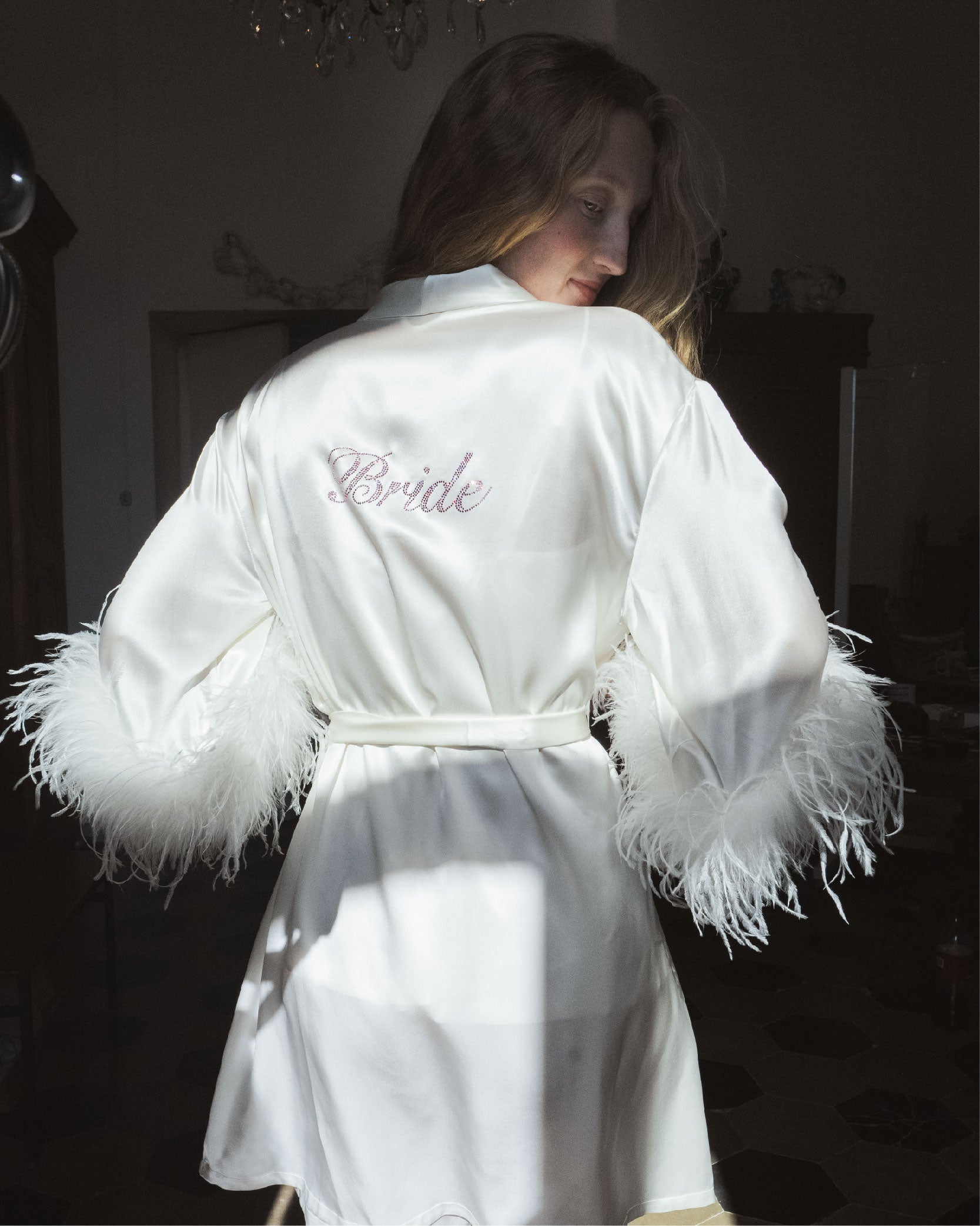 White satin robe with feather trim and 'Bride' embroidery on a dark background