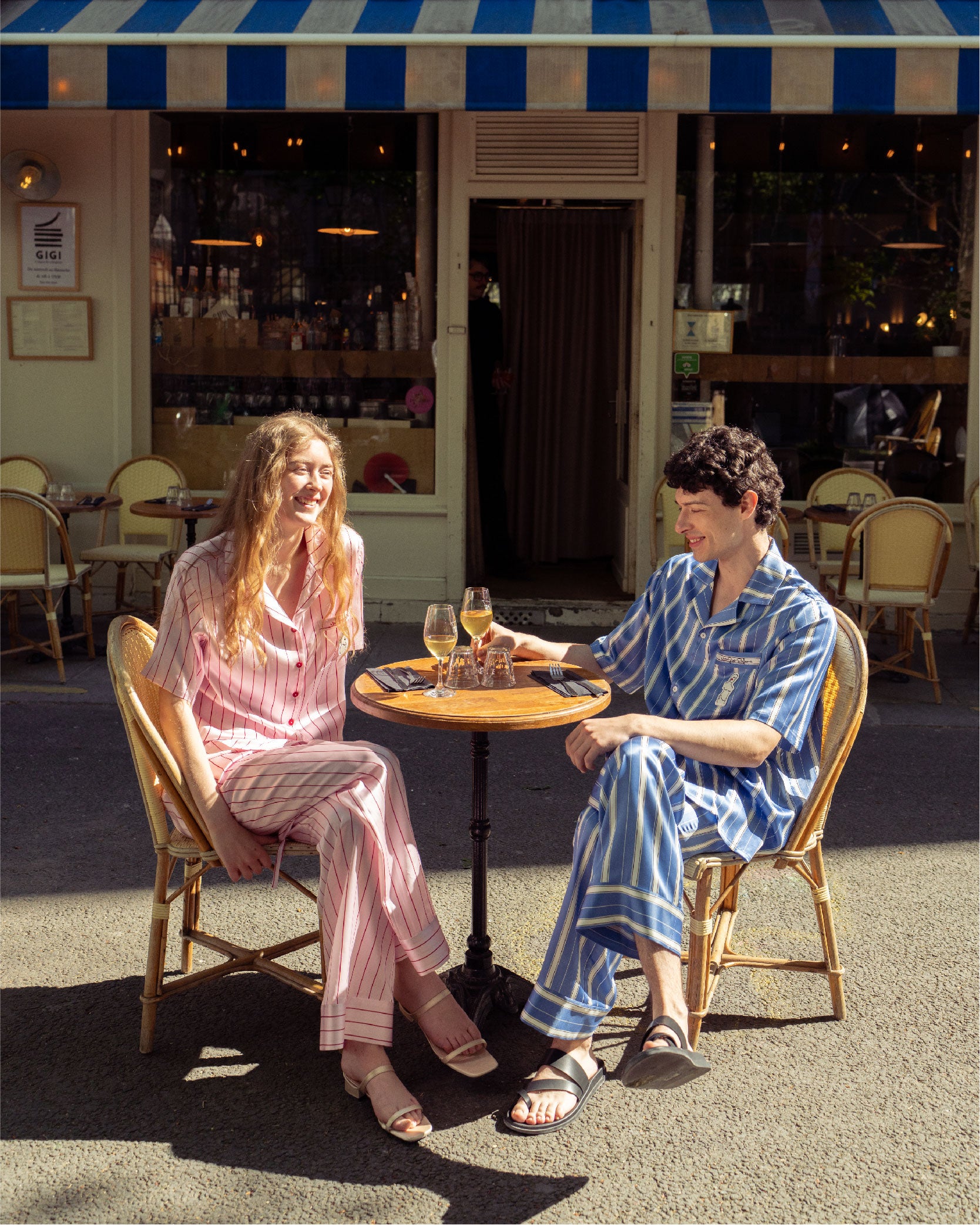 Two people sitting at a table under a striped awning, possibly in a cafe or restaurant.