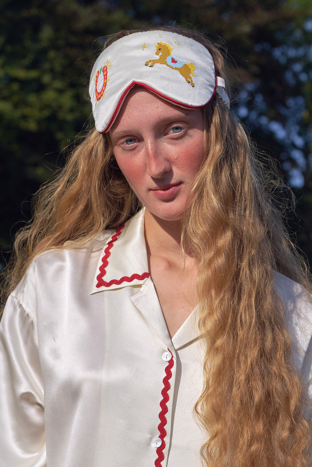 Woman wearing a white headband with a horse design, long blonde hair, and a white shirt with red trim.