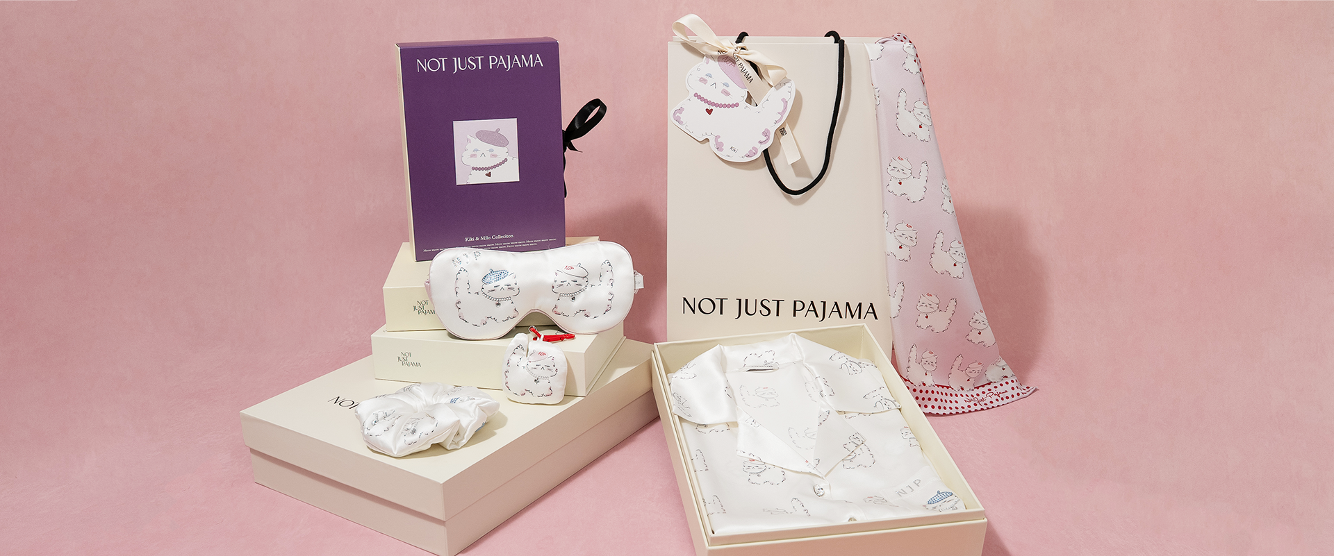 White silk pajama set with packaging and accessories on a pink background
