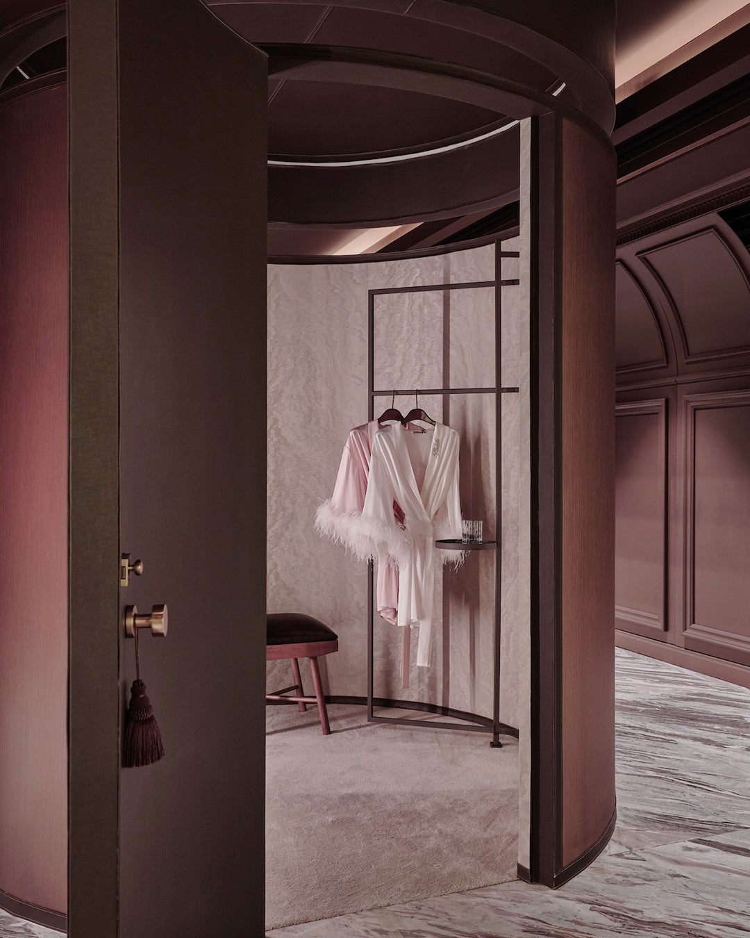 Luxurious interior with a robe hanging on a rack in a room with pink walls and marble floor.